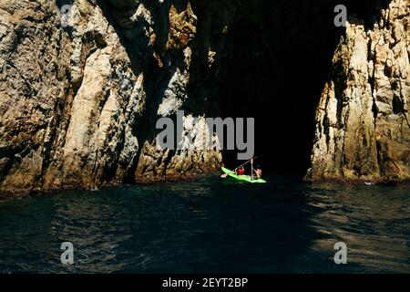 Selektiver Fokus - Vater und Sohn rudern in einem Kanu, um eine natürliche Höhle im Mittelmeer zu betreten, an einem sonnigen Sommertag. Sie genießen beide. Stockfoto