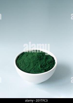 Spirulina Pulver in einer weißen Schale auf blauem Hintergrund mit Platz für Text. Superfood-Konzept. Vertikale Ausrichtung. Stockfoto