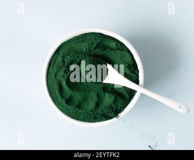 Chlorella Pulver in einer weißen Schüssel mit einem Teelöffel auf blauem Hintergrund. Superfood-Konzept. Horizontale Ausrichtung. Draufsicht. Stockfoto