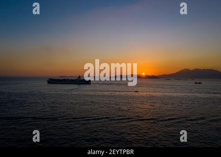 Frachtschiff passiert Victoria Harbour bei Sonnenuntergang Stockfoto