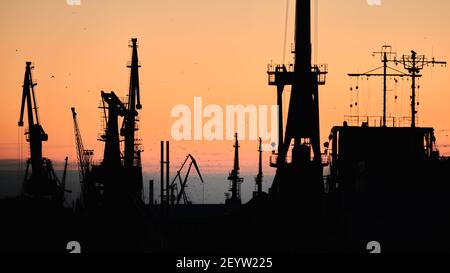 Silhouetten von Schiffen und Containerkranen im Seehafen, Sonnenuntergang Hintergrund. Landschaft Industrielandschaft. Stockfoto