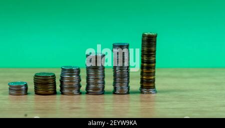 Ersparnisse, zunehmende Spalten von Gold und Silber Münzen isoliert auf grünem Hintergrund Stockfoto