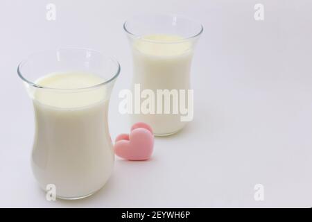 Zwei transparente Gläser mit weißem cremigen italienischen Dessert Panna Cotta auf hellem Hintergrund. Kleine niedliche rosa Herz zwischen zwei Tassen Stockfoto