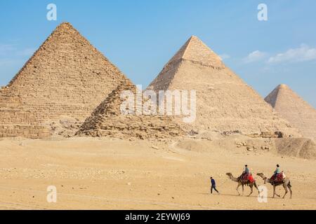 Ein lokaler Reiseleiter führt zwei Touristen auf Kamelen um die Pyramiden von Gizeh, Gizeh Plateau, Groß-Kairo, Ägypten Stockfoto