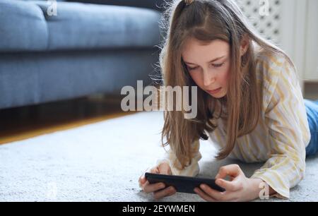 Tween Mädchen mit Smartphone auf dem Teppich liegen. Stockfoto