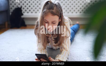 Tween Mädchen mit Smartphone auf dem Teppich liegen. Stockfoto