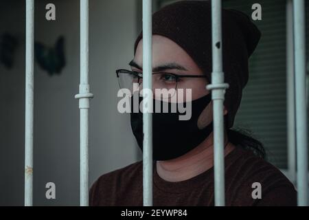 Nahaufnahme eines kaukasischen Männchens in Gläsern und Gesichtsmaske hinter Gittern im Gefängnis - neues normales Konzept Stockfoto