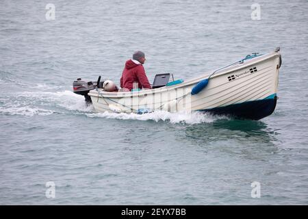 Ein Mann in einem kleinen Holzboot mit einem Motor fährt in den Hafen von Porthleven, Cornwall Stockfoto