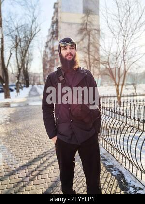 Porträt eines jungen bärtigen Europäers im Winter Jacke und Hut Spaziergänge in einer verschneiten Winterstadt Stockfoto