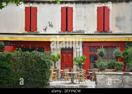Provençal Restaurantfassade mit verwitterter Stuckwand und leuchtend roten Fensterläden in Saint-Rémy-de-Provence, Frankreich. Stockfoto