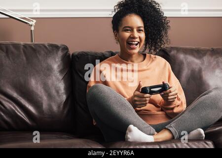 Glückliche junge Frau, die einen Spielcontroller auf dem Sofa hält Stockfoto