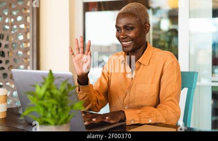 Glückliche afrikanische ältere Frau mit Spaß dabei Videoanruf mit Laptop in der Bar Restaurant Stockfoto