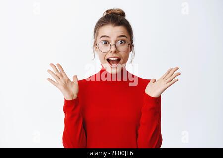 Portrait von aufgeregt schöne Unternehmerin in Gläsern die Hände hoch und keuchen erstaunt, hören gute Nachrichten und suchen erstaunt, stehend in rot Stockfoto