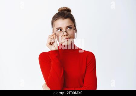 Nachdenkliche, gut aussehende Frau in Brille denkend, rechts auf leeren Raum schauend und nachdenkend, nachdenklich stehend vor weißem Hintergrund Stockfoto