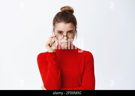 Bild von nachdenklichen und selbstbewussten blonde Frau berühren Brillenrahmen und ernsthaft auf die Kamera schauen, Annahme machen, denken an starren Sie an Stockfoto