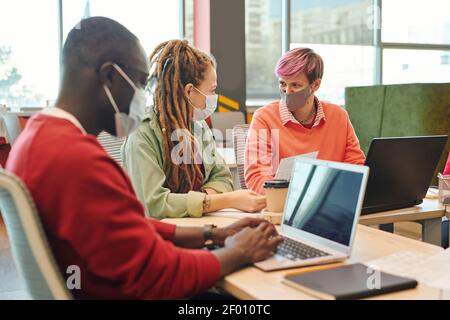 Zwei junge, zeitgenössische Geschäftsfrauen in der Beratung zu Casualwear und Schutzmasken Über einige Arbeitspunkte beim Sitzen am Schreibtisch Stockfoto