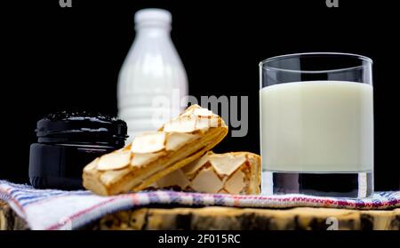 Stillleben einer Flasche Milch mit einem Glas gefüllt mit Milch und Gebäck, Marmelade mit Milch auf schwarzem Hintergrund. Milchprodukt. Stockfoto