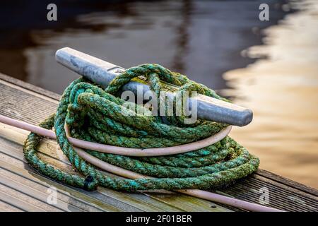 Seil um einen Metallbollard gebunden, der auf einem hölzernen festgemacht ist Steg Stockfoto