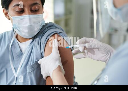 Behandeltes Klinikpersonal, das ihrer Mischrassenweibin Injektionen verabreicht Kollege während der Impfung in der medizinischen Büro der zeitgenössischen Kliniken Stockfoto