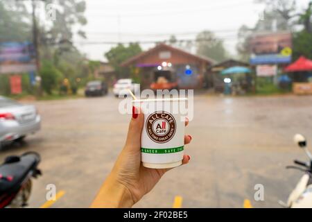 Genießen Sie heißen Kaffee unter dem Dach eines lokalen thailändischen Lebensmittelladens, während Sie auf den tropischen Regen warten Stockfoto