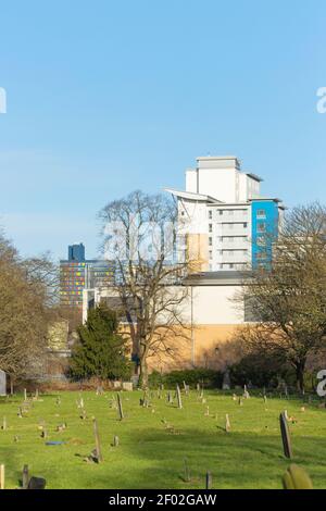 Zeigt Grabsteine seitlich im Vordergrund, dann im Hintergrund St. George’s Tower und die University of Leicester: Opal Court. Stockfoto