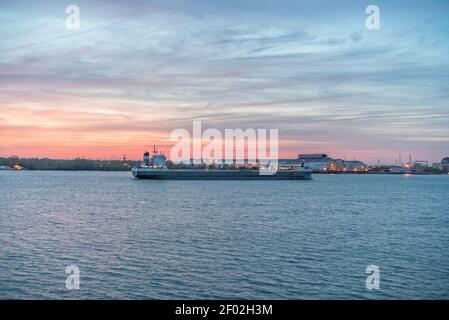 Ein großes Industrieschiff segelt im Meer unter der wolkiger Himmel während des Sonnenuntergangs Stockfoto