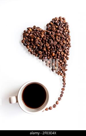 Für eine süße Kaffeepause. Ein Herz aus Kaffeebohnen, das wie ein kleiner Ballon aus einer Tasse auf weißem Hintergrund fliegt. Stockfoto