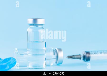 Impfstoff, Spritze und OP-Handschuh. Zwei Flaschen Impfstoff und Spritze auf blauem Hintergrund. Impfstoff und medizinisches Konzept Stockfoto
