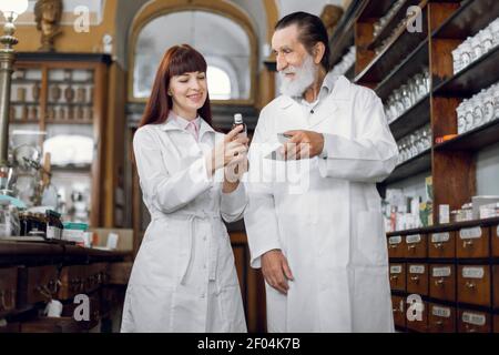 Zwei Apotheker, älterer Mann und junge Frau, die in der alten Apotheke arbeiten. Apotheker und Apotheker prüfen die Qualität der Medikamente und vergleichen zwei Stockfoto