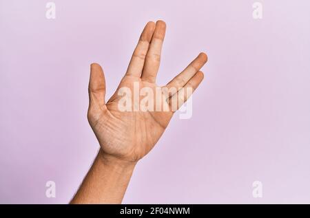 Arm und Hand des kaukasischen jungen Mannes über rosa isolierten Hintergrund Gruß tun vulcan Salute, zeigt Hand Handfläche und Finger, Freak Kultur Stockfoto