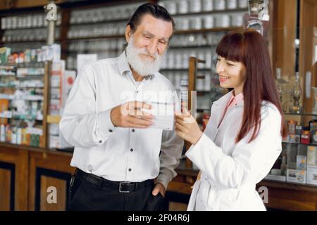 Professionelle schöne weibliche Apothekerin im Gespräch mit männlichen Senior Client, während er ihm die Box mit Pillen. Apotheker mit Kunde in alt Stockfoto