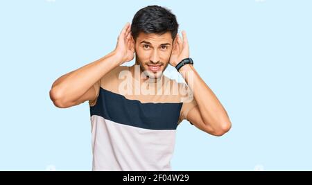 Junger schöner Mann trägt Freizeitkleidung versucht, beide Hände auf Ohr Geste hören, neugierig auf Klatsch. Hörproblem, taub Stockfoto