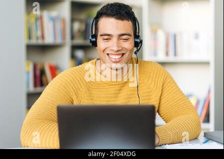Selbstbewusster männlicher Mitarbeiter bei Online-Videotreffen. Gutaussehend lächelnd hispanic Freiberufler Kerl verwendet Laptop, trägt Kopfhörer, diskutieren Arbeitsfragen mit Kollegen Stockfoto