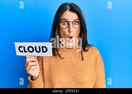 Mittlere Alter Brünette Frau hält Papier mit Wolke Wort erschrocken und erstaunt mit offenem Mund für Überraschung, Unglauben Gesicht Stockfoto
