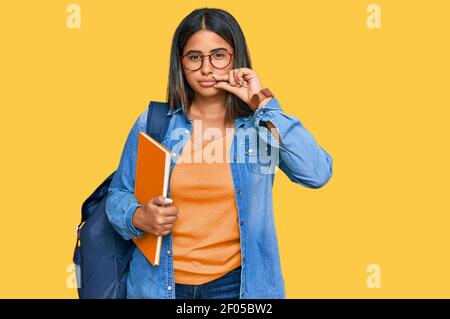 Junge lateinische Mädchen tragen Student Rucksack und hält Bücher Mund und Lippen geschlossen als Reißverschluss mit den Fingern. Geheim und leise, Tabu reden Stockfoto