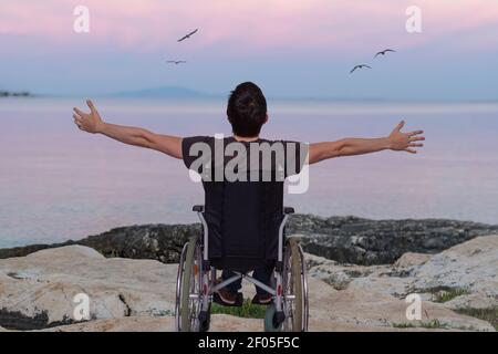 Behinderter Mann im Rollstuhl in Strandnähe bei Sonnenuntergang. Stockfoto