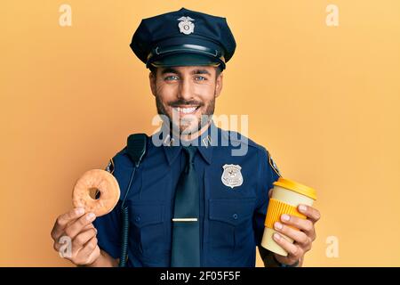 Schöner hispanischer Polizeimann, der Donut isst und Kaffee trinkt, lächelt mit einem glücklichen und kühlen Lächeln im Gesicht. Zähne zeigen. Stockfoto