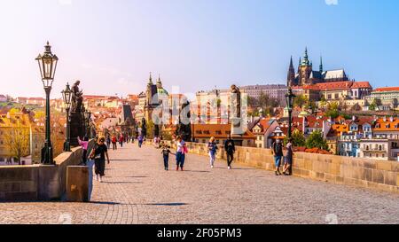PRAG, TSCHECHISCHE REPUBLIK - 17. APRIL 2020: Menschen mit Gesichtsmasken auf der Karlsbrücke in Prag. Panorama der Prager Burg. Pandemie des Coronavirus Stockfoto