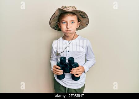 Kleiner kaukasischer Junge Kind trägt Explorer Hut hält Fernglas puffing Wangen mit lustigen Gesicht. Mund mit Luft aufgeblasen, Luft fangen. Stockfoto