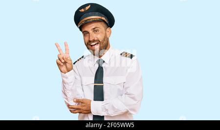 Schöner Mann mit Bart tragen Flugzeug Pilot Uniform lächelnd mit glücklichem Gesicht zwinkend an der Kamera tun Siegeszeichen. Nummer zwei. Stockfoto