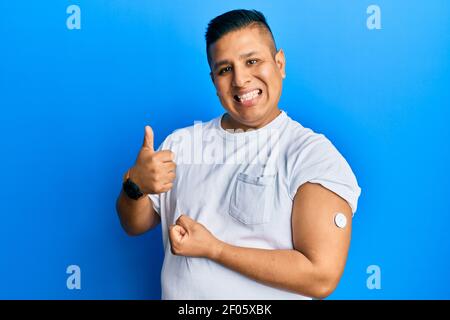 Junge lateinische Mann mit Glucose-Meter-Taste lächelt glücklich und positiv, Daumen nach oben tun ausgezeichnet und Zustimmung Zeichen Stockfoto