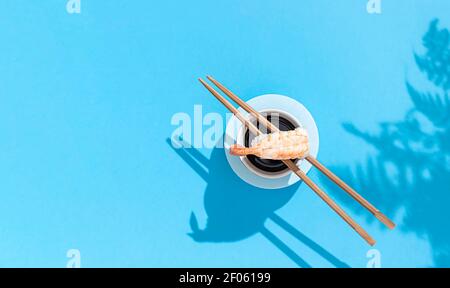 Nigiri Garnele in der Nähe von Sojasauce, mit Essstäbchen auf blauem Hintergrund. Hartes Licht und Schatten. Traditionelle japanische Küche. Speisekarte im Restaurant, Sushi-Bar Stockfoto