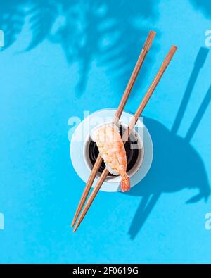 Nigiri Garnele in der Nähe von Sojasauce, mit Essstäbchen auf blauem Hintergrund. Hartes Licht und Schatten. Traditionelle japanische Küche. Speisekarte im Restaurant, Sushi-Bar Stockfoto