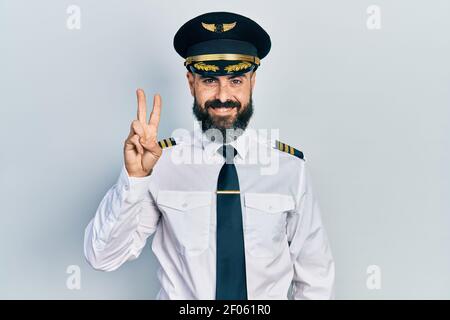 Junge hispanische Mann trägt Flugzeug Pilot Uniform zeigt und zeigt mit den Fingern Nummer zwei, während lächelnd zuversichtlich und glücklich. Stockfoto