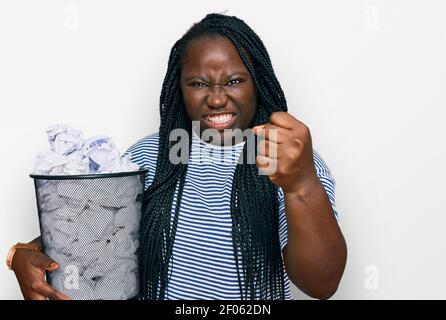 Junge schwarze Frau mit Zöpfen, die Papierbehälter voller zerknitterter Papiere hielten, verärgert und frustriert, vor Wut schreiend, verrückt vor Wut und Hand schreiend Stockfoto