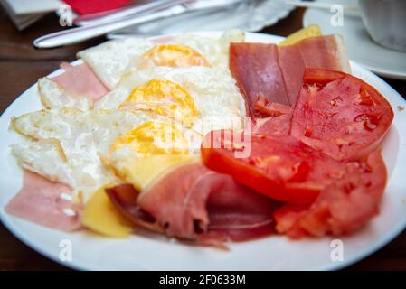 Spiegeleier, Speck, Tomaten, Schinken und Kaffee in einer Tasse mit Besteck und Servietten.Salz und Pfeffer im Hintergrund. Stockfoto