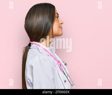 Schöne hispanische Frau trägt Arzt Uniform und Stethoskop Blick zur Seite, entspannen Profil Pose mit natürlichen Gesicht mit selbstbewussten Lächeln. Stockfoto