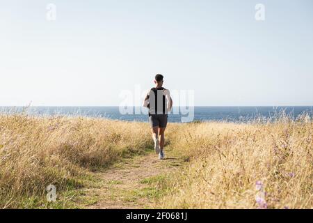 Muskulöser Rüde-Jogger läuft beim Training auf der Wiese entlang Auf dem Hintergrund des Meeres im Sommer Stockfoto