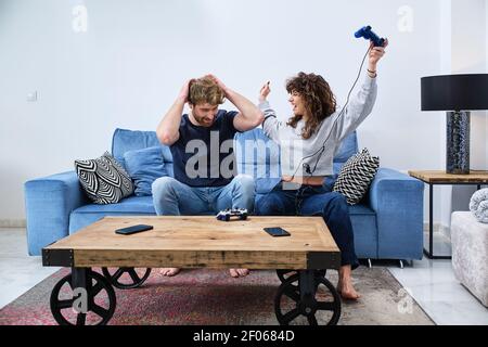 Fröhliche und aufgeregt junge Paar in legerer Kleidung spielen Video Spiel auf Konsole im stilvollen Wohnzimmer Stockfoto