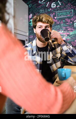 Junge fröhliche Paar in hellen Freizeitkleidung im gemütlichen Gespräch Küche und einander beim Kaffee betrachten Stockfoto